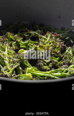 Purple sprouting broccoli frying in a deep ceramic frying pan background backdrop. Stock Photo