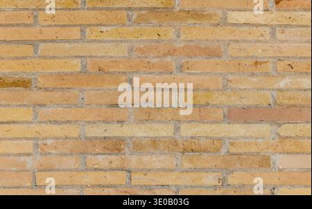 Photograph of a yellow-beige brick wall showing horizontal masonry lines, subtle weathering and varied tones, ideal as a background texture for archit Stock Photo