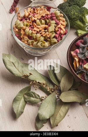 Italian pasta in bowls and laurel leaf on white wood Stock Photo