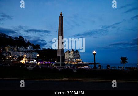Light fades as evening falls on the seafront with the Cenotaph, lights on the pier and a floodlit Grand Hotel, Llandudno, North Wales. Stock Photo