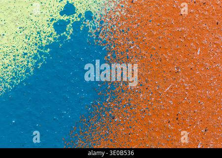 Macro close-up of a wall spray painted in blue, yellow and orange. Abstract full frame textured splattered graffiti background with copy space. Stock Photo