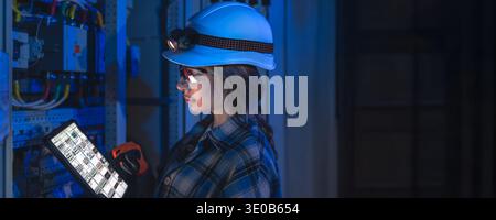 Female technician inspecting electrical panel with tablet. Technician digital monitoring. Stock Photo