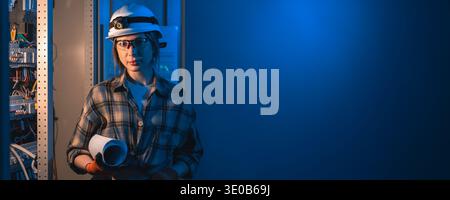 Engineer with blueprints standing near electrical panel in blue light. Engineer energy control. Stock Photo