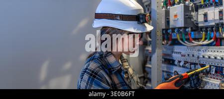 Female repairing electrical panel with screwdriver in technical room. Electrician service safety. Stock Photo