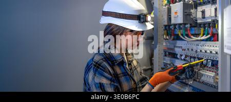 Female electrician repairing electrical panel with screwdriver industrial room. Electrician service. Stock Photo