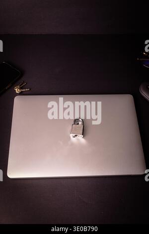 Padlock on a closed laptop with keys on a dark desk, conceptual image of cybersecurity, device protection, privacy and data security at home office. Stock Photo