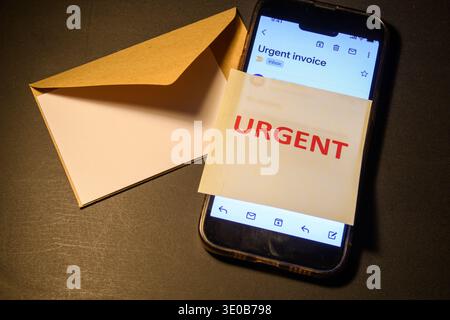Smartphone showing an urgent invoice email beside an envelope, conceptual image of phishing, scam, fraud, spam and cybersecurity risk in digital commu Stock Photo