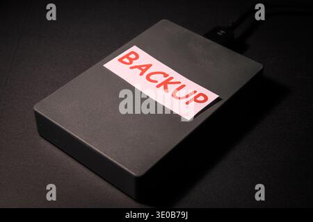 External hard drive labeled backup on a dark desk, conceptual image of data backup, storage, disaster recovery and cybersecurity protection. Stock Photo