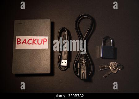 External backup drive with cables, padlock and keys on a dark desk, conceptual image of secure backup, protected storage, encryption and data security Stock Photo
