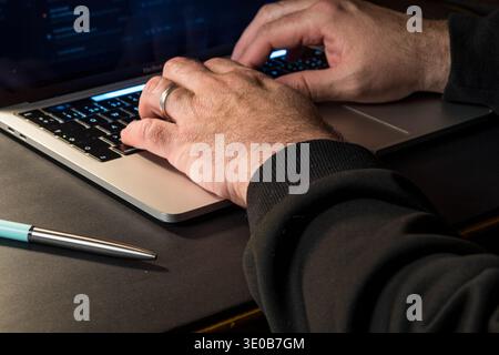 Close up of hands typing on a laptop at a dark desk, conceptual image of login activity, computer security, remote work and digital access. Stock Photo