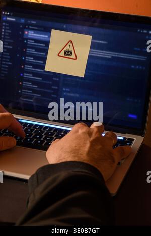 Hands using a laptop with a phishing warning symbol on screen, conceptual image of email scam, suspicious message, cyber threat and online fraud. Stock Photo