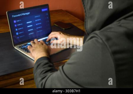 Password manager screen on a laptop with a hooded user typing, conceptual image of credential security, password storage, account protection and cyber Stock Photo
