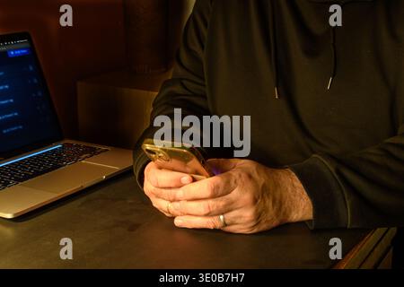 Person holding a smartphone next to a laptop, conceptual image of mobile authentication, secure access, password management and cybersecurity. Stock Photo