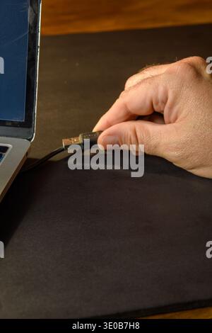 Hand plugging a USB cable into a laptop, conceptual image of device connection, data transfer, external access, hardware security and digital workflow Stock Photo