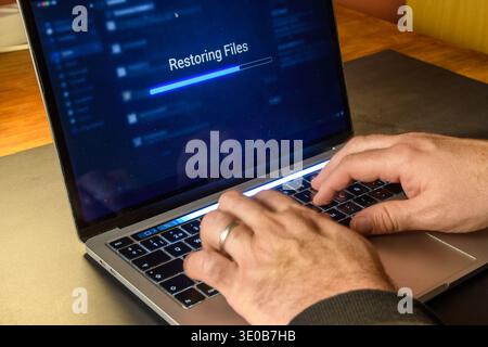 Hands on a laptop showing restoring files and a progress bar, conceptual image of data recovery, backup restoration, cybersecurity and system recovery Stock Photo