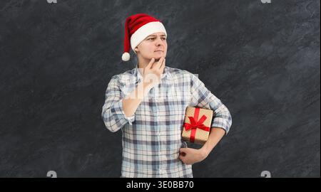 Pensive young man in santa hat with gift Stock Photo