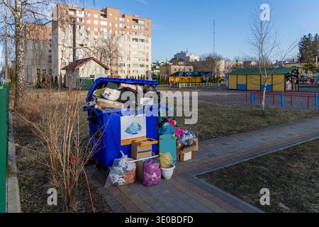Overflowing trash container in residential neighborhood. Overfilled blue garbage bin beside apartments and a playground, showing urban waste problems Stock Photo