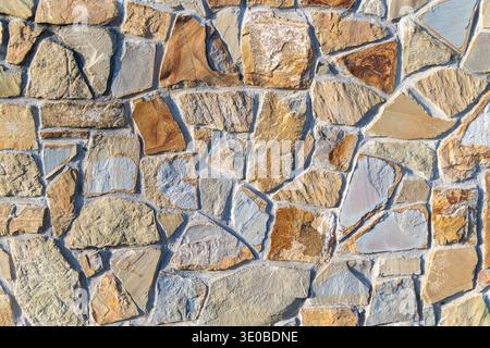 Rustic stone wall texture background. Close-up of an irregular natural stone wall with warm earthy tones and visible mortar, ideal for construction Stock Photo