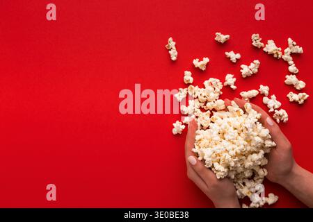 Heap of popcorn in hands on red background, top view Stock Photo