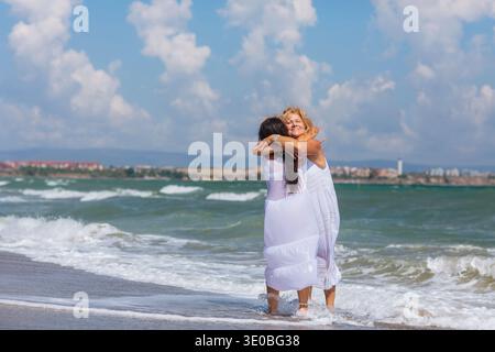 Two Women Hugging on Beach in Ocean Waves Stock Photo