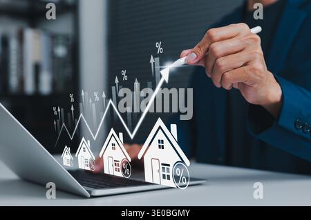 Real estate market growth concept with businessman using laptop and pointing at rising financial graph with house icons and percentage signs. Stock Photo