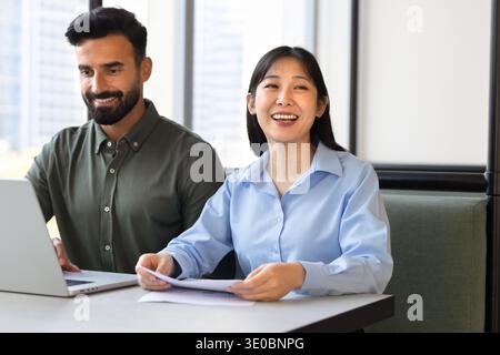 Cheerful colleagues sit at coworking desk with laptop and documents Stock Photo