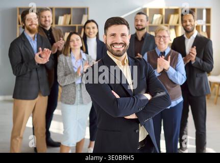 Confident young businessman with applauding team in office for career growth Stock Photo