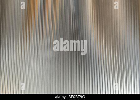 A textured metallic surface with vertical ribbed patterns and subtle hints of warm orange light reflecting on the corrugated metal Stock Photo