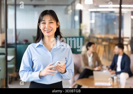 Portrait of smiling businesswoman holding smartphone in office Stock Photo