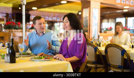 Cheerful adult interracial couple having dinner in restaurant Stock Photo