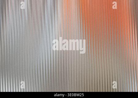 A textured metallic surface with vertical ridges, featuring a gradient from silver to a warm orange hue, creating a visually striking abstract backgro Stock Photo