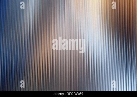 A textured metallic surface with vertical ribbed lines, reflecting warm and cool light in a gradient Stock Photo