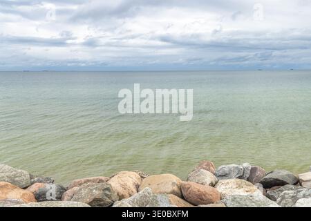 The coast of the Baltic Sea in northern Poland. Calm water stretches to the horizon beneath a cloudy sky, bordered by rocky shoreline. Serene coastal Stock Photo