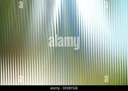 The textured surface of frosted glass creates a beautiful abstract pattern with vertical lines and a soft gradient of green and blue hues Stock Photo