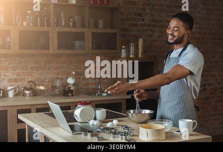 Black man baking pastry and using laptop in kitchen Stock Photo