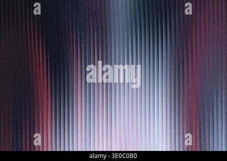 A textured glass surface with vertical ridges, illuminated by a gradient of dark blue to light blue and hints of red, creating an abstract and moody a Stock Photo