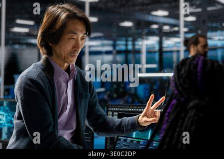 Teamworking data center senior engineer and coworker deploying servers. Asian IT professional and colleague in server room managing large scale IT infrastructure rackmounts Stock Photo
