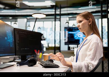 Young female programmer in office using AI scripts, automating repetitive tasks. Junior developer using artificial intelligence technology to speed up feature implementation Stock Photo