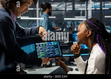 Close up of manager guiding intern in server farm with hardware supporting data mining. Team leader and trainee doing internship in data center, learning to do maintenance on racks using tablet Stock Photo