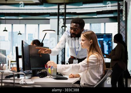 Lead programmer providing support to new worker using PC in software development agency. African american IT expert helping trainee coding during internship in tech startup Stock Photo
