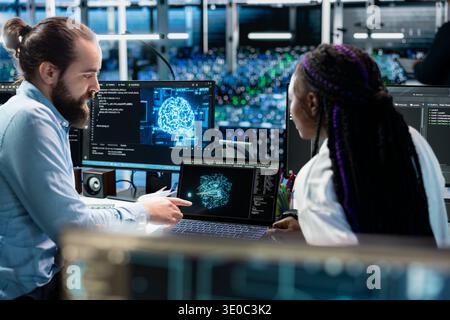 Data center team leader teaching intern to monitor AI applications, adjusting machine learning parameters. Server hub mentor and woman doing internship enhance artificial intelligence Stock Photo