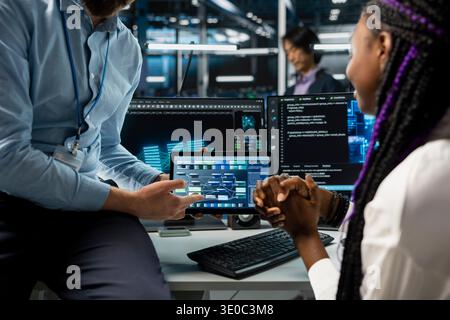 Close up of programmers coding on tablet in data center, using machine learning tech. IT professionals using device in server room, managing automation scripts for optimized operations Stock Photo