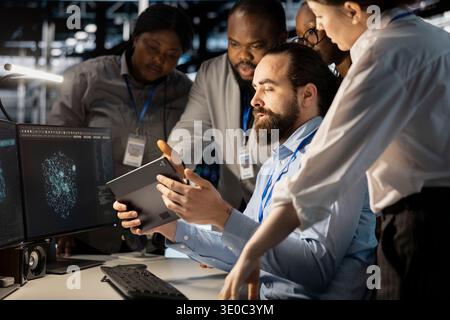 Team of software developers using computer in server farm, analyzing data. Data center office coworkers examining equipment using devices, ensuring system integrity and security Stock Photo