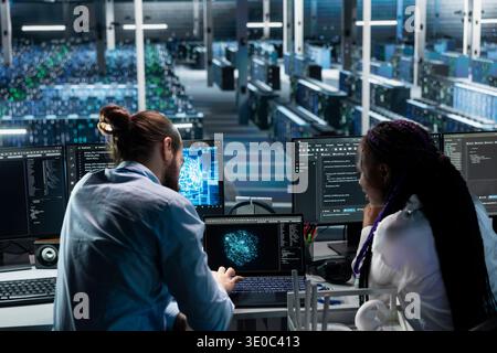 Server hub team leader helping intern optimize supercomputers performance with AI assistant analysis. Data center manager and young woman using LLM chatbot suggestions to speed up tasks Stock Photo