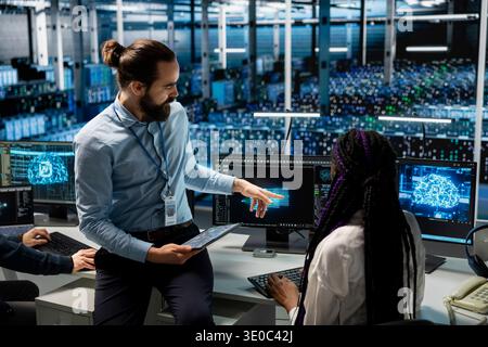 Manager supervising female engineer in data center coding with generative AI assistance. Supervisor oversees work by IT specialist leveraging artificial intelligence large language model Stock Photo