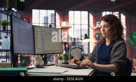 Software expert at workstation programming on pc and writing lines of code, using coding tools and a terminal window interface. Woman debugging software for web development. Camera A. Stock Photo