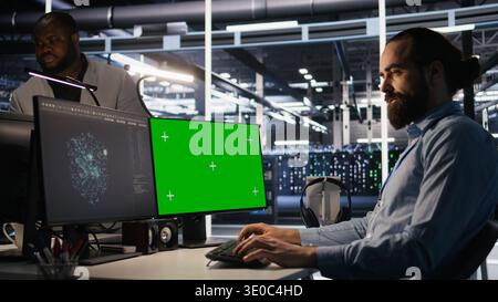 Data center technician doing software updates using green screen mockup computer. Server room IT specialist , optimizing infrastructure using chroma key isolated screen PC, camera A Stock Photo