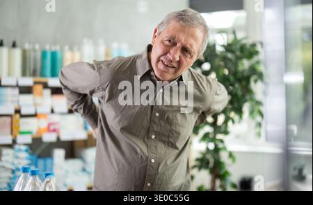 Older man experiencing sharp back pain while shopping in pharmacy Stock Photo