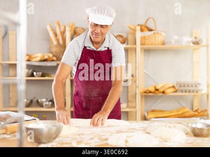 Senior man works as baker in bakery, molds pies from dough, creates croissants from dough. Stock Photo