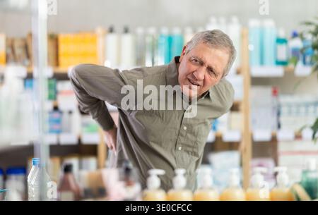 Older man experiencing sharp back pain while shopping in pharmacy Stock Photo